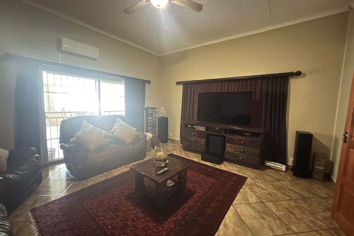A comfortable living room featuring tiled flooring, a ceiling fan, and a wall-mounted air conditioning unit, with sliding door access to the patio.