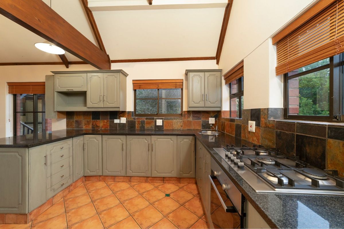 A spacious kitchen featuring sage green cabinetry, dark granite countertops, a built-in gas hob, and vaulted ceilings with exposed timber beams.