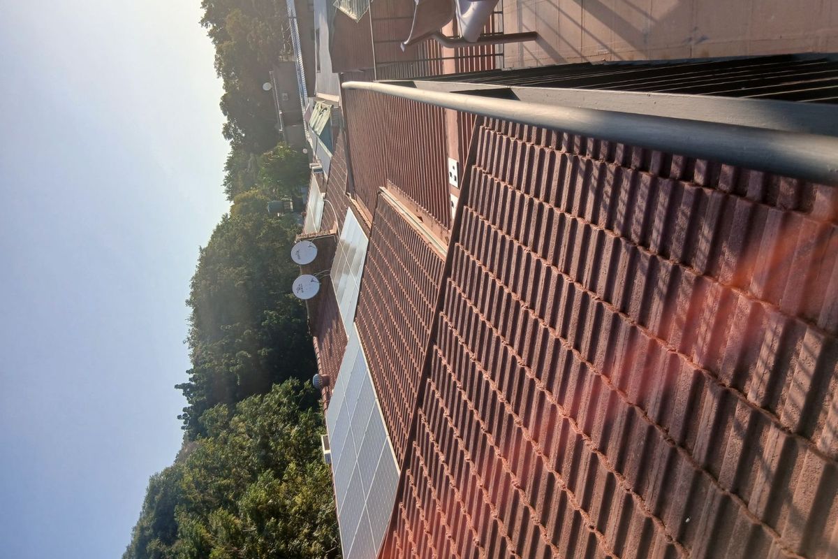 An elevated view of the property's tiled roof featuring installed solar panels and satellite dishes, overlooking a wooded area.