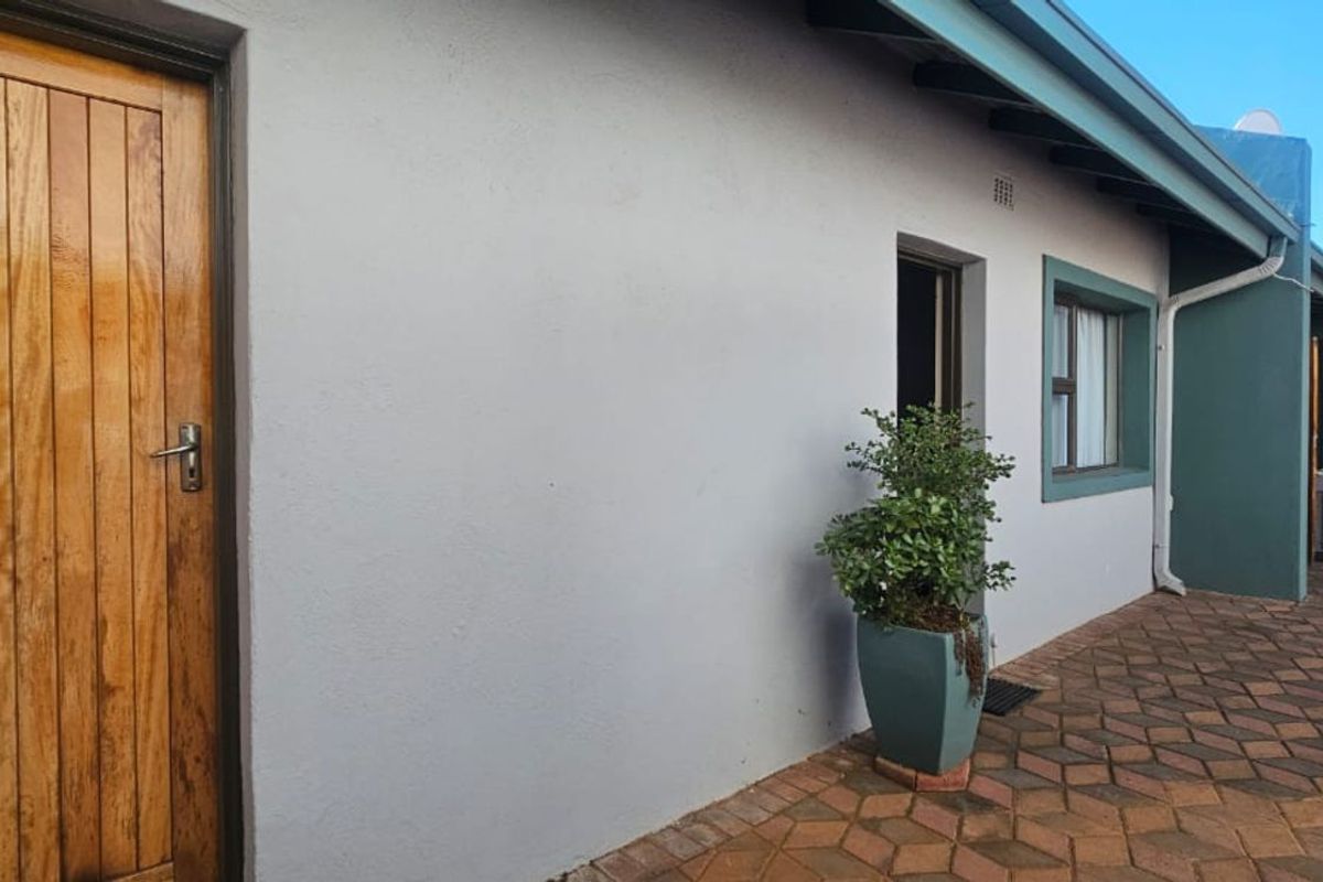 A view of the rear exterior of the house featuring a paved patio area, a wooden door, and painted exterior walls.