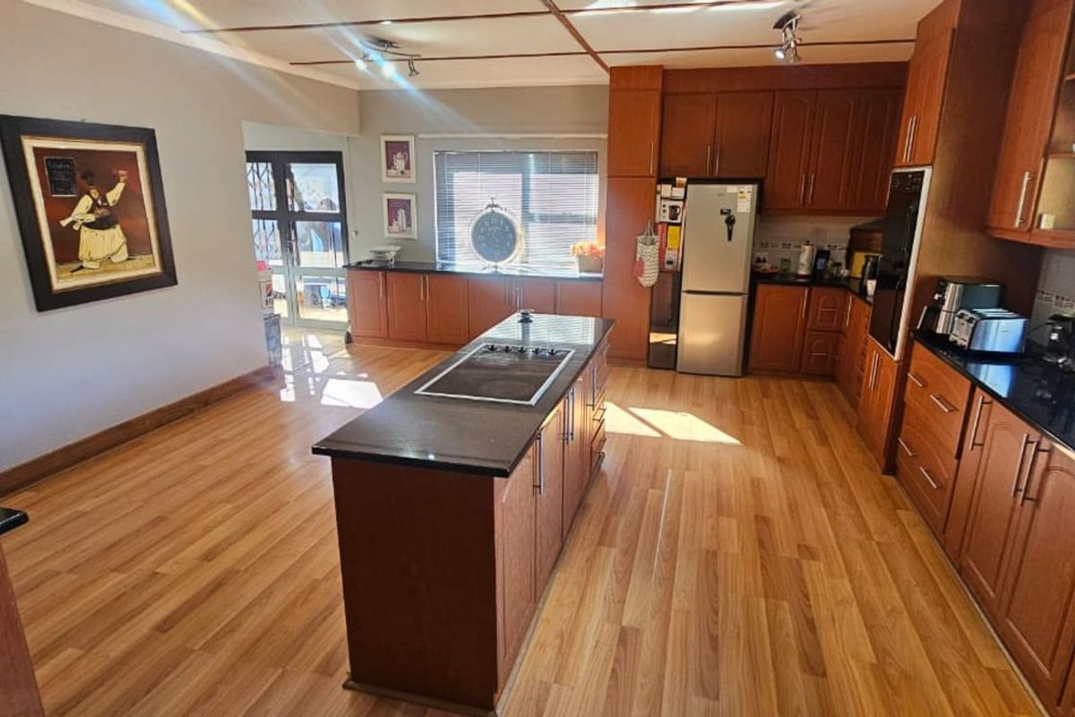 Spacious kitchen featuring dark wood cabinetry, granite countertops, a central island with a built-in hob, and laminate flooring.