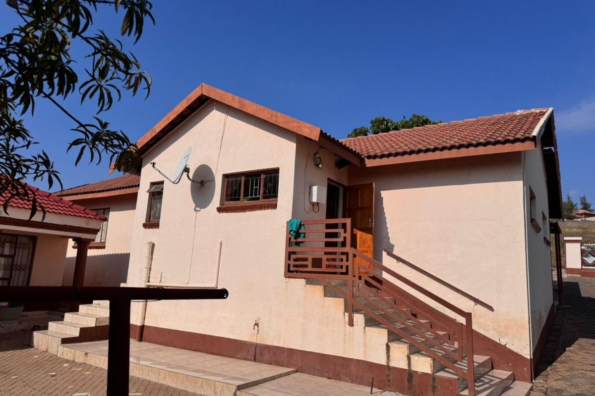 Exterior view of a residential house featuring a tiled roof, staircase with metal railings, and paved outdoor area.