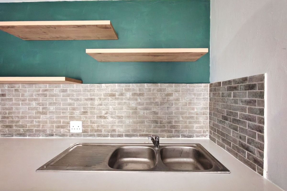 A functional kitchen sink area featuring a stainless steel double basin, subway tile backsplash, and modern floating timber shelves against a green accent wall.