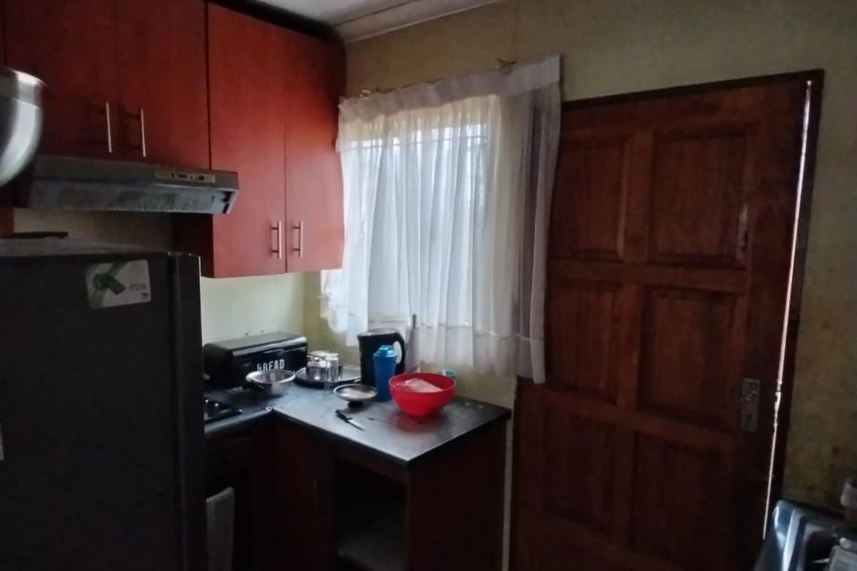 A compact kitchen featuring wooden cabinetry, a built-in extractor fan, and tiled flooring, providing a functional workspace with direct access to an exterior door.