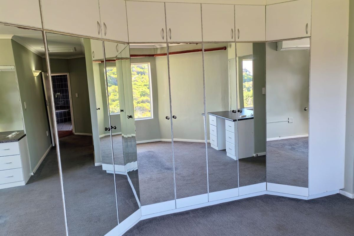 Spacious bedroom featuring extensive floor-to-ceiling mirrored built-in cupboards, integrated vanity desk, and neutral wall tones with carpeted flooring.