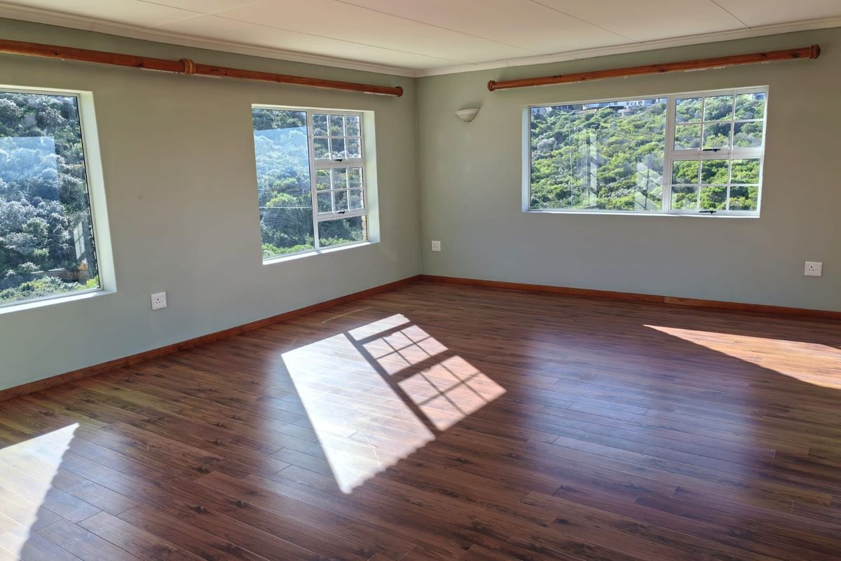 A bright, empty living room featuring wood-look laminate flooring, neutral walls, and large windows offering scenic views of the surrounding greenery.