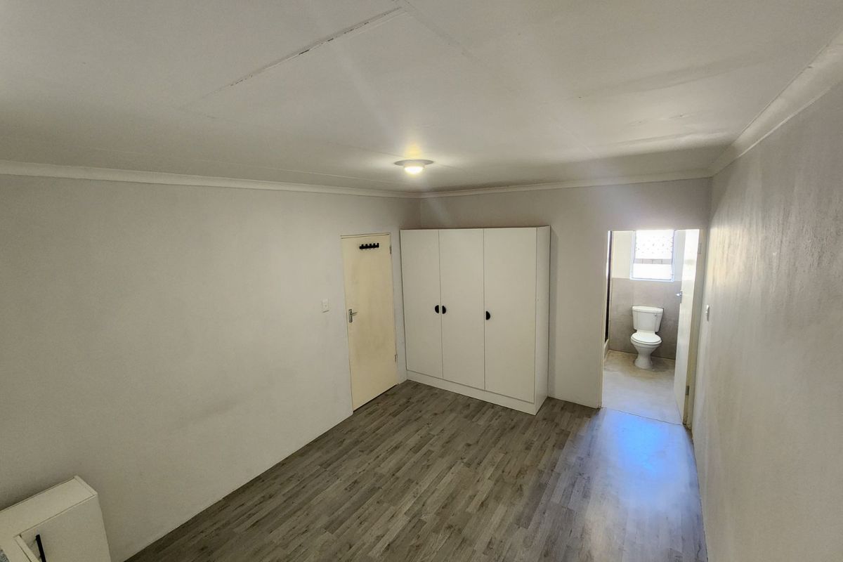 A bedroom featuring wood-look laminate flooring, built-in wardrobe, and an en-suite bathroom with a toilet visible through the doorway.