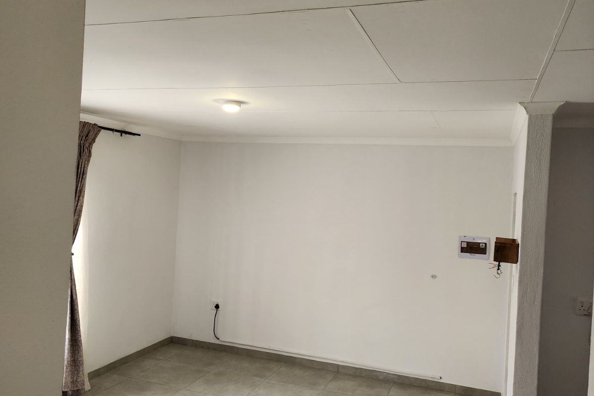 A bright, empty living area featuring neutral floor tiles, white walls, and a simple ceiling finish, offering a versatile space for customization.