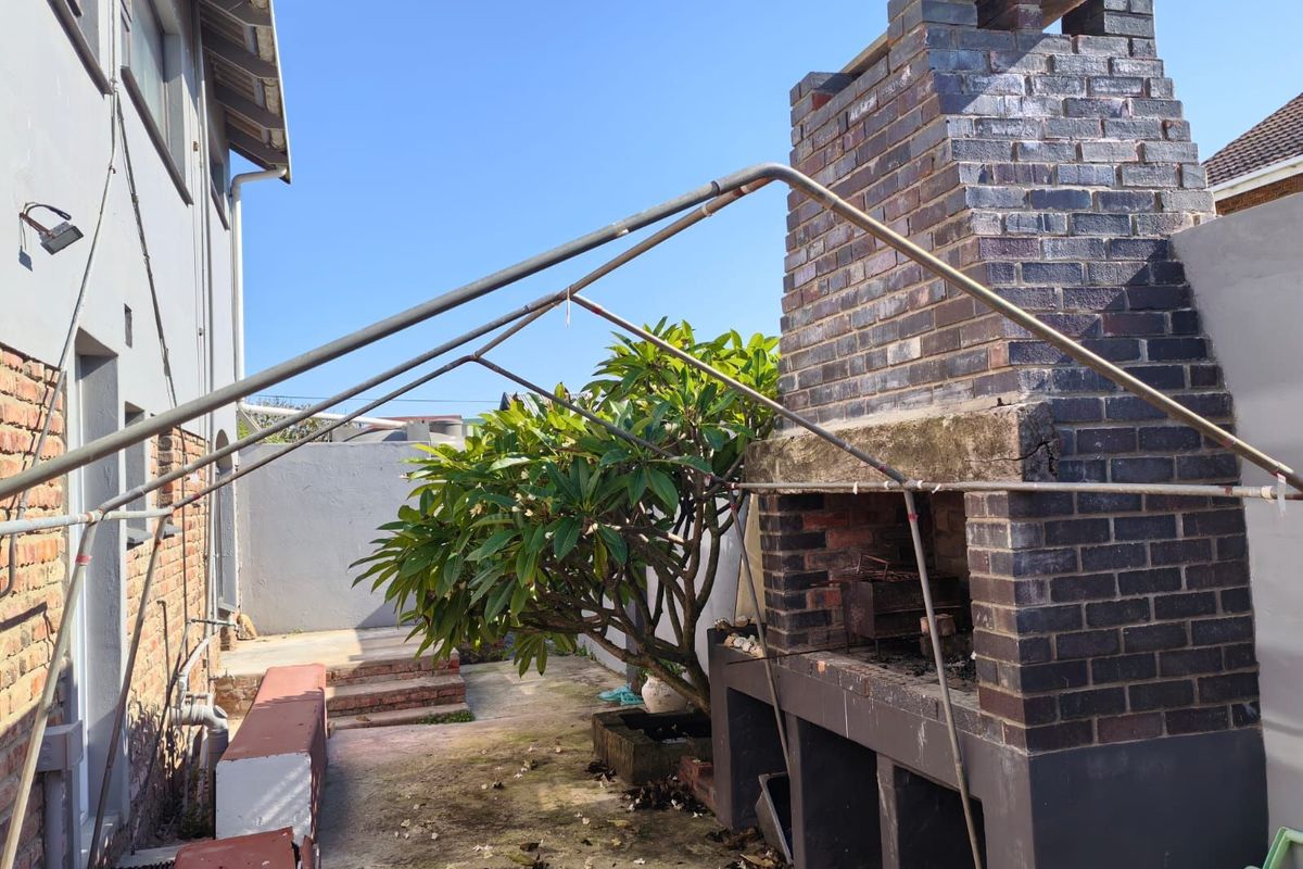 Outdoor entertainment area featuring a large built-in brick fireplace and a metal frame structure, set within a paved rear courtyard space.