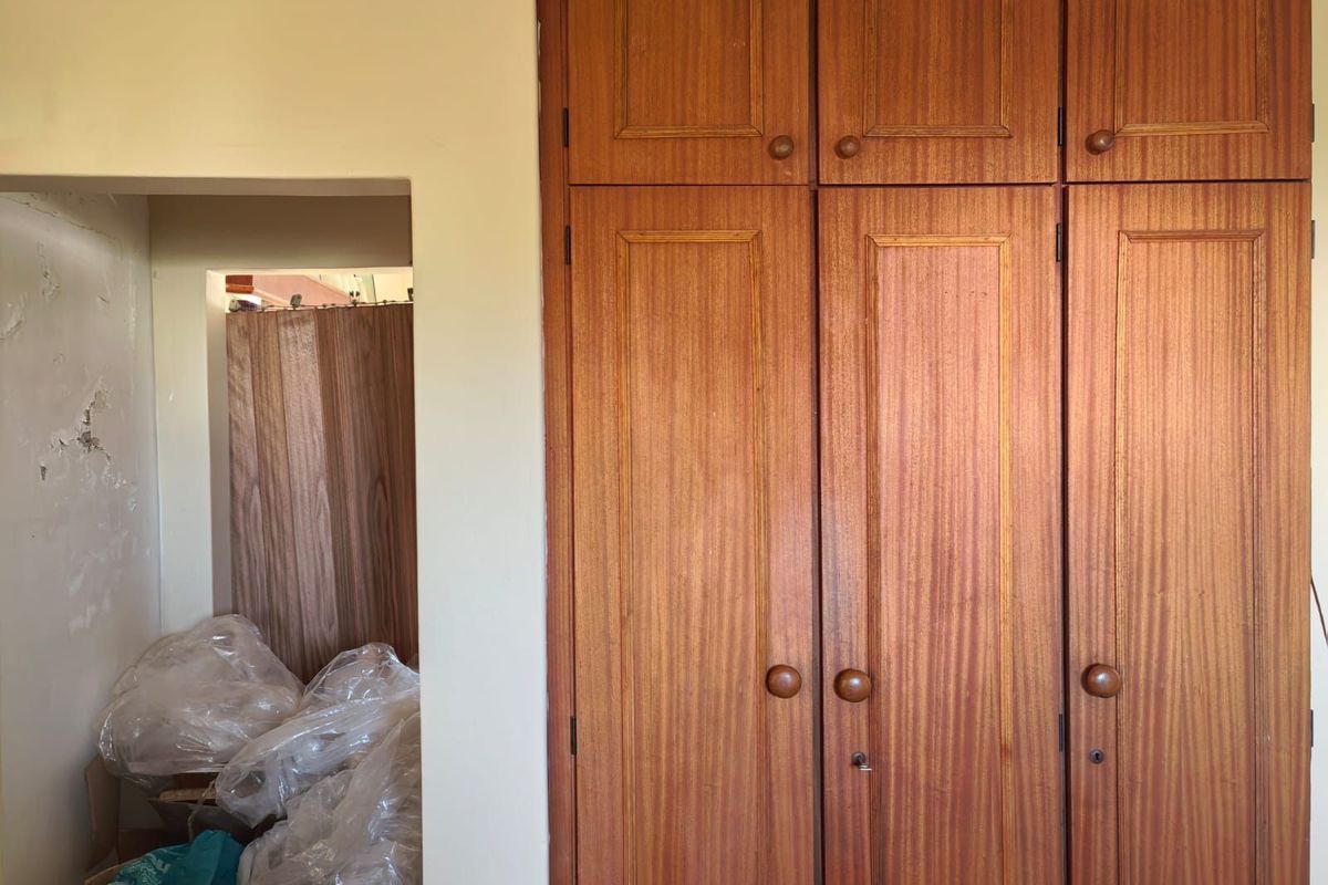 A bedroom featuring built-in wooden cabinetry and an adjacent alcove area showing signs of wall surface deterioration.