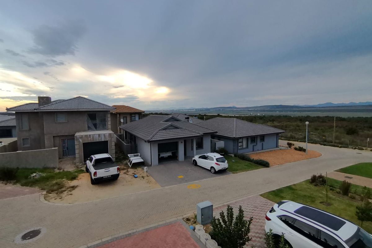 An elevated view of a residential townhouse complex featuring paved driveways, tiled roofs, and surrounding landscaped grounds under a cloudy sky.