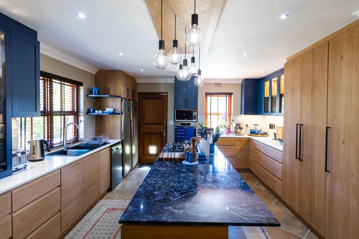 Modern kitchen featuring a large central island with dark stone countertop, custom wood cabinetry, integrated appliances, and stylish pendant lighting.