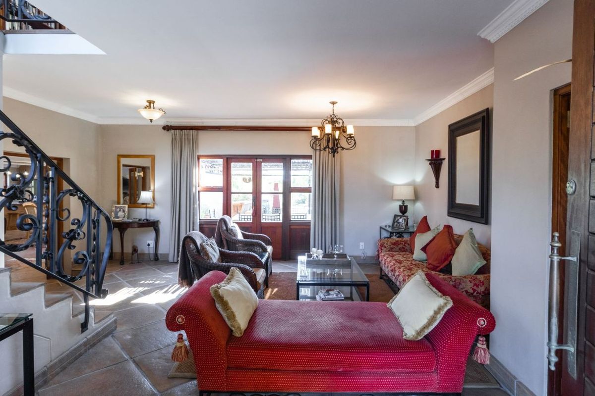 Spacious living room featuring tiled flooring, a decorative wrought iron staircase, and French doors leading to the outdoor area.