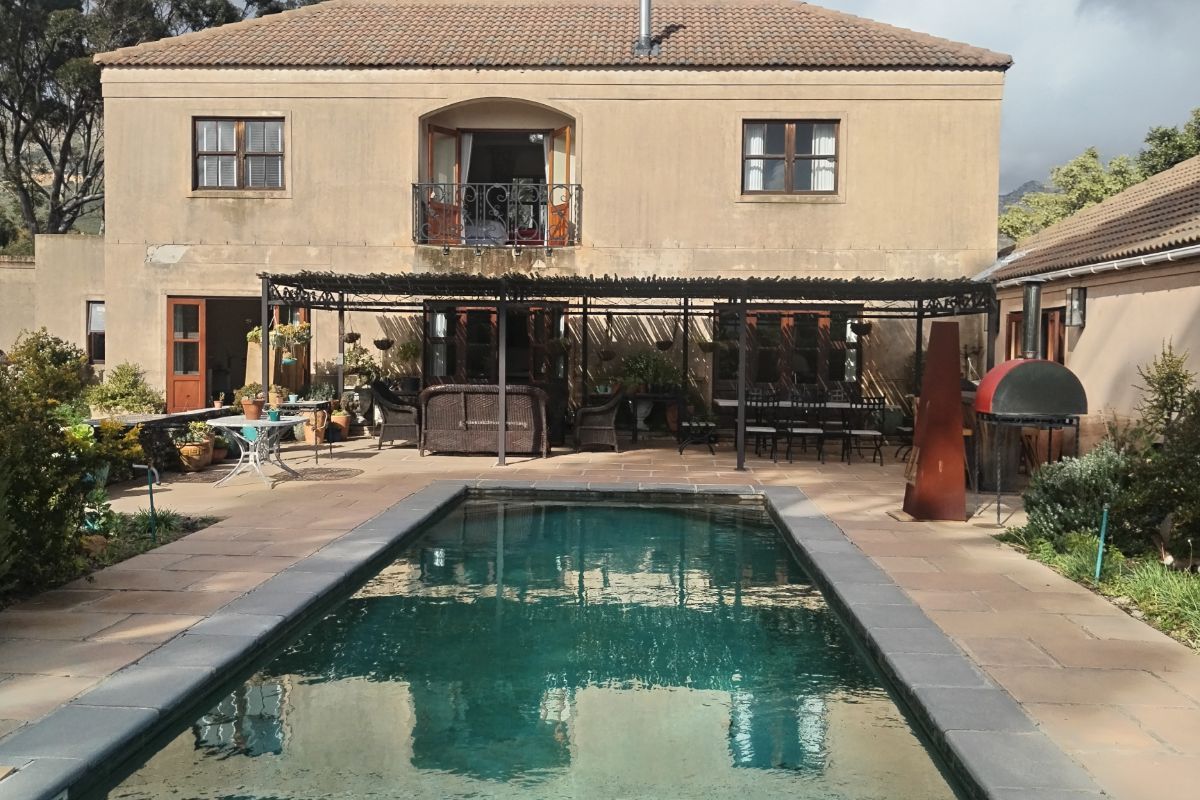Rear view of a two-story house featuring a swimming pool, paved patio area with a pergola, and a second-floor balcony.