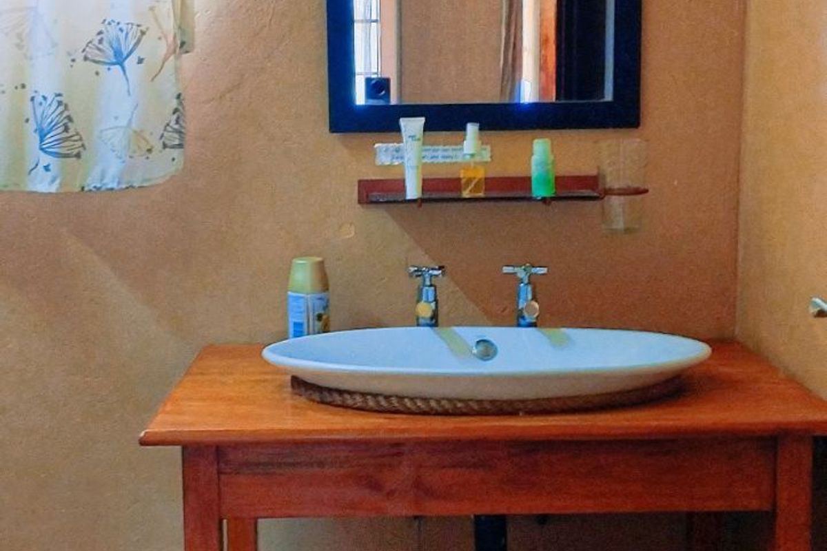 A rustic bathroom vanity featuring a vessel sink set on a wooden slatted stand with a wall-mounted mirror.