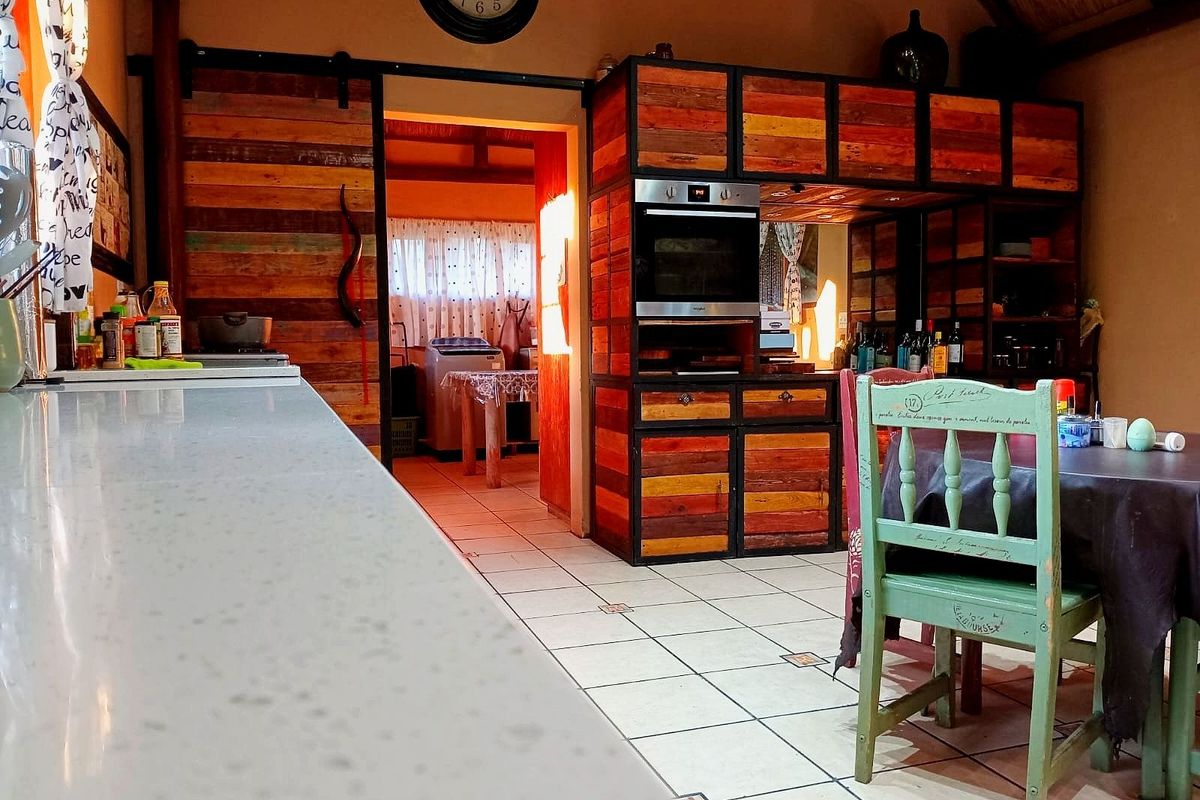 Rustic kitchen featuring custom timber cabinetry, built-in oven, and tiled flooring, with an open-plan layout leading to an adjacent utility area.