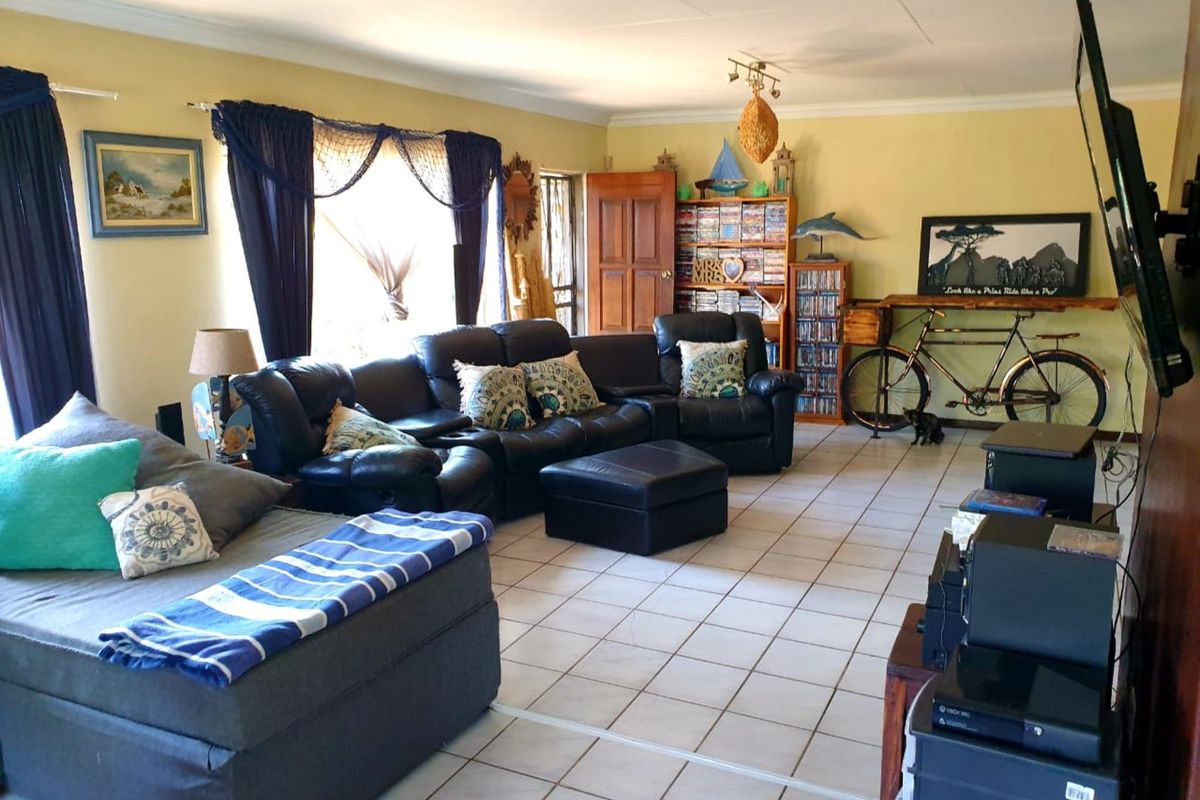 A spacious living room featuring light-colored ceramic floor tiles, coved ceilings, and a large window with natural light.
