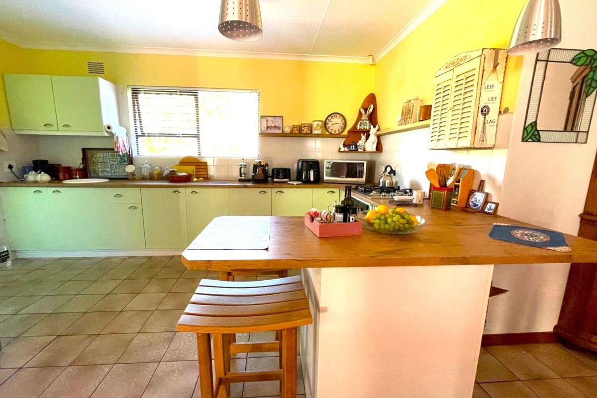 A functional kitchen featuring light green cabinetry, a wooden breakfast bar, tiled flooring, and ample counter space for meal preparation.