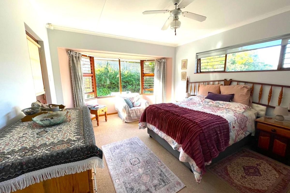 A spacious bedroom featuring a large bay window, ceiling fan, and neutral wall finishes, offering a comfortable and well-lit living space.