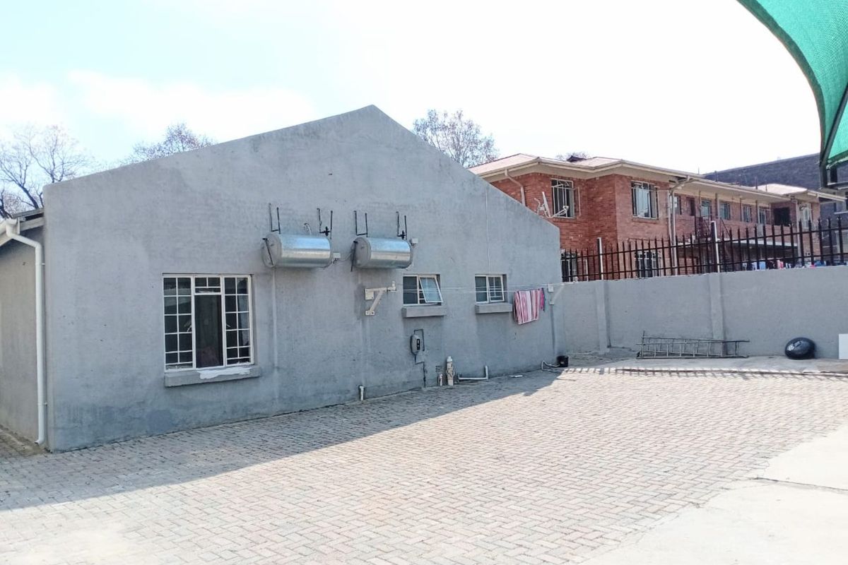 Rear exterior view of the townhouse featuring a paved courtyard, grey rendered wall finish, and external wall-mounted geysers.