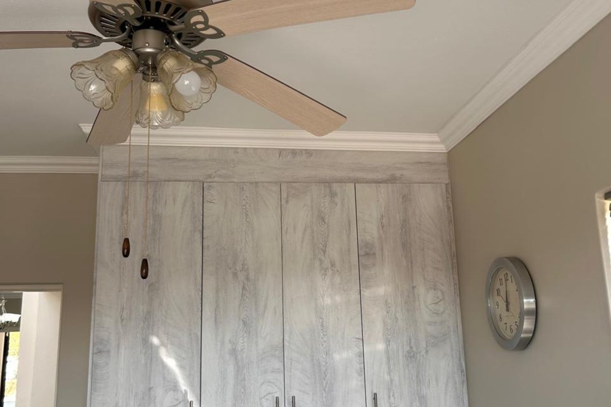 Bedroom featuring built-in light wood-grain cabinetry with integrated drawers and a ceiling fan with light fixture.