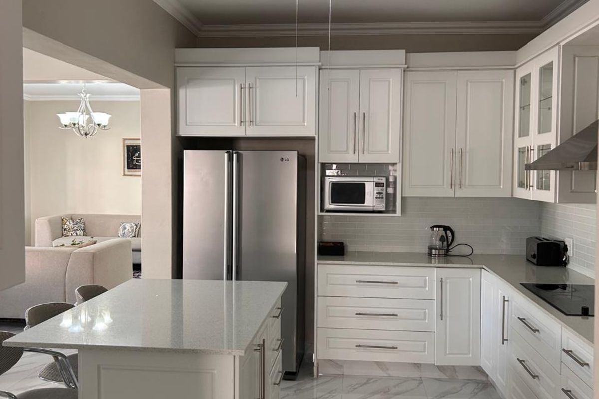 Modern kitchen featuring white cabinetry, stone countertops, a central island, built-in microwave, and sleek marble-look floor tiles, seamlessly flowing into the adjacent living area.