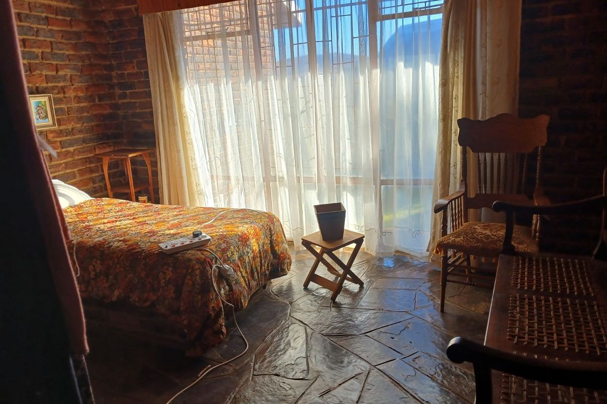 A rustic bedroom featuring exposed brick walls and traditional flagstone flooring, with large windows providing natural light.