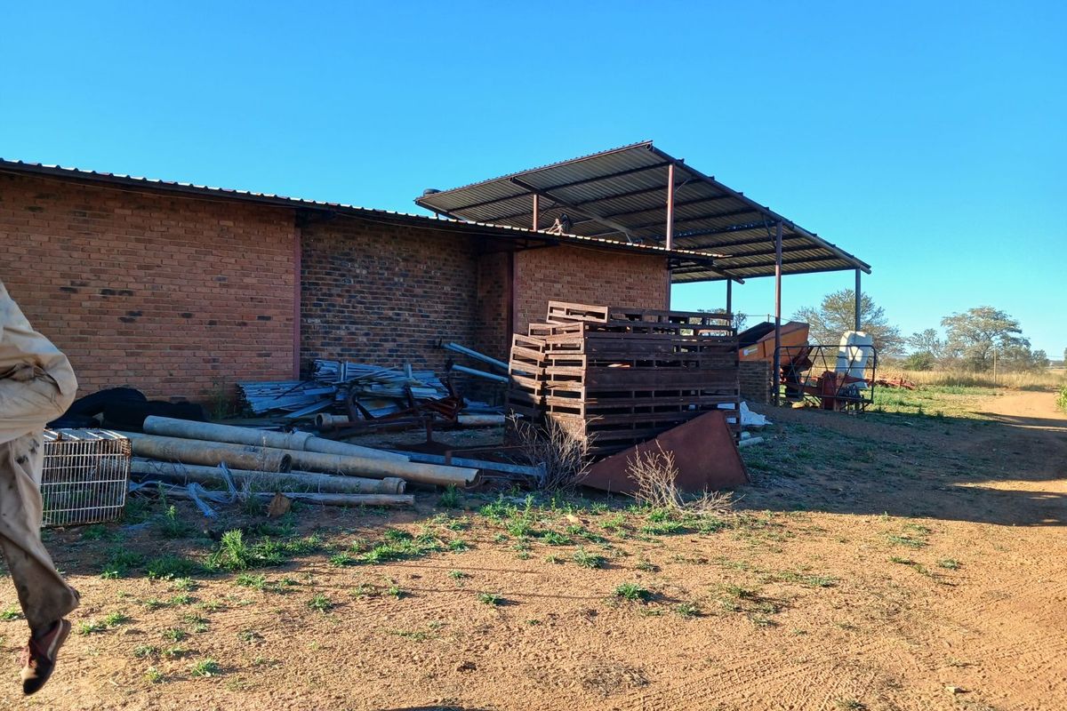 Exterior view of a farm building featuring a brick structure with an attached metal-roofed lean-to storage area.