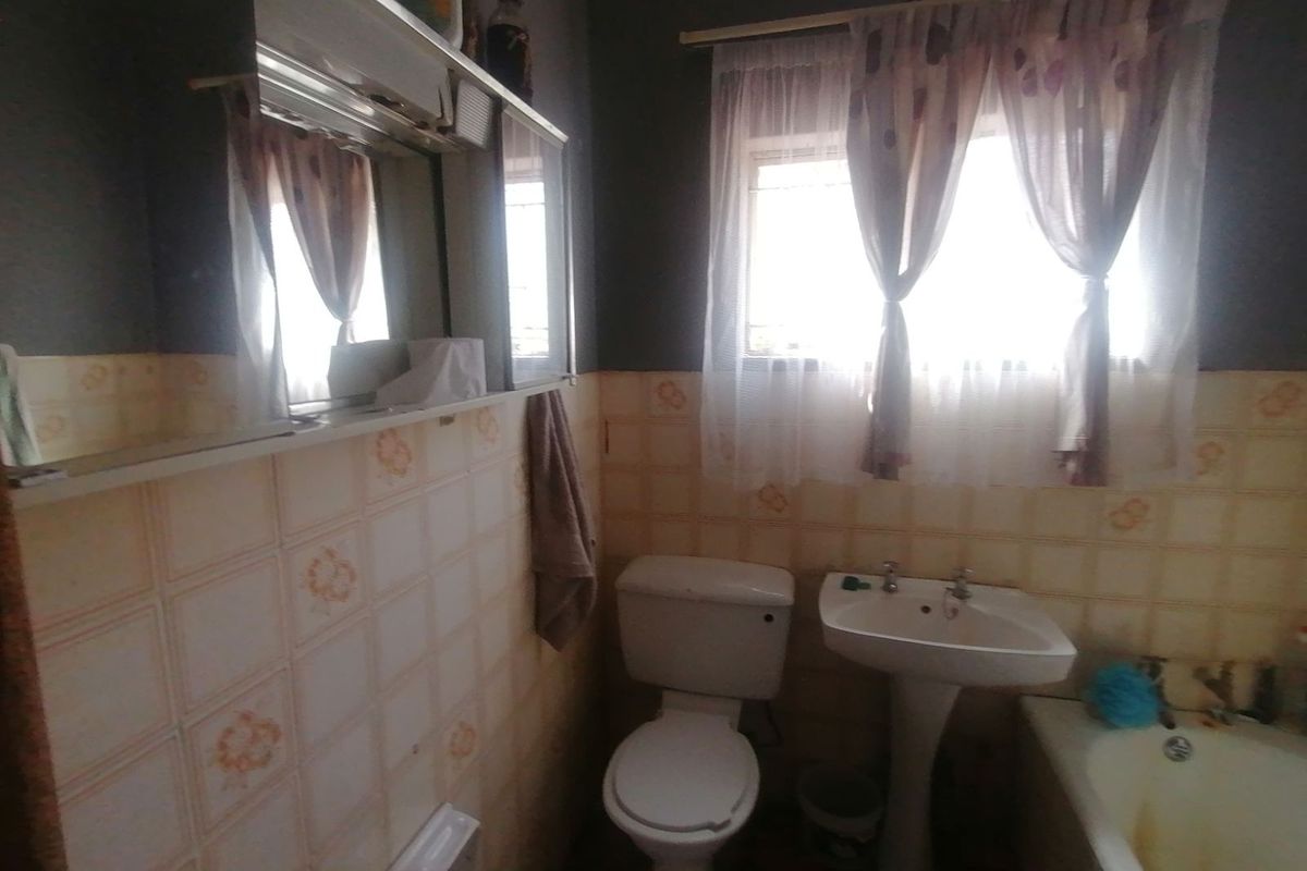A dated bathroom featuring a pedestal sink, toilet, and bathtub with original wall tiling and a built-in vanity mirror.
