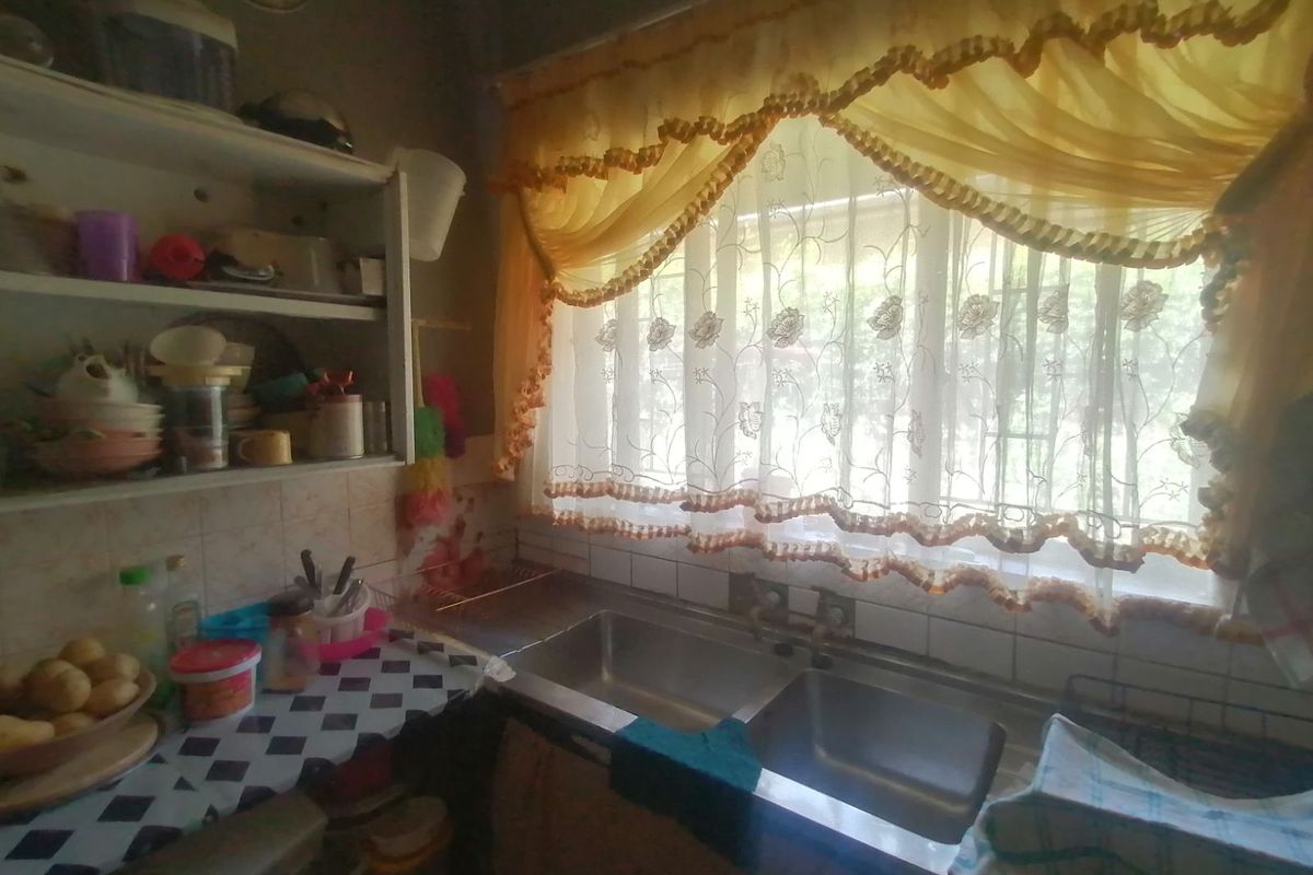 A functional kitchen area featuring a double stainless steel sink, tiled splashbacks, and open shelving storage.