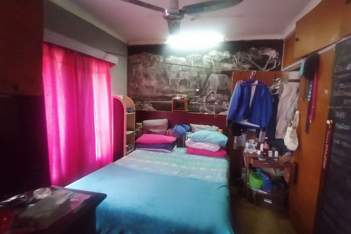 A bedroom featuring a ceiling fan, built-in storage cabinetry, and a large wall mural, offering a functional space with potential for modernization.