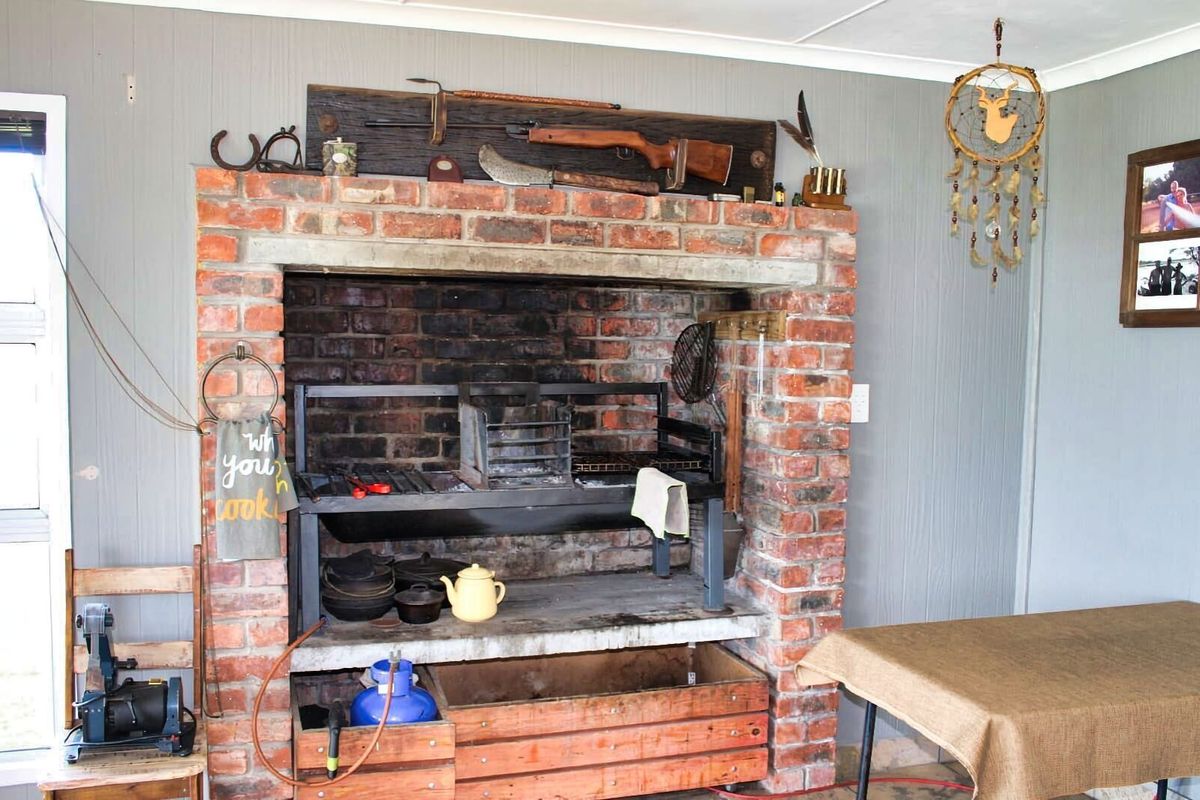 A rustic indoor braai area featuring a traditional brick-built fireplace with integrated metal grill and hearth.