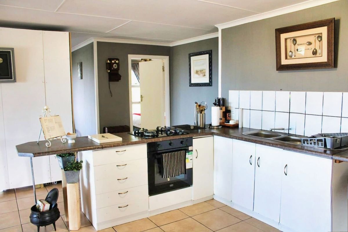 A functional kitchen featuring white cabinetry, a built-in oven, gas hob, and tiled splashbacks, with an integrated breakfast counter.