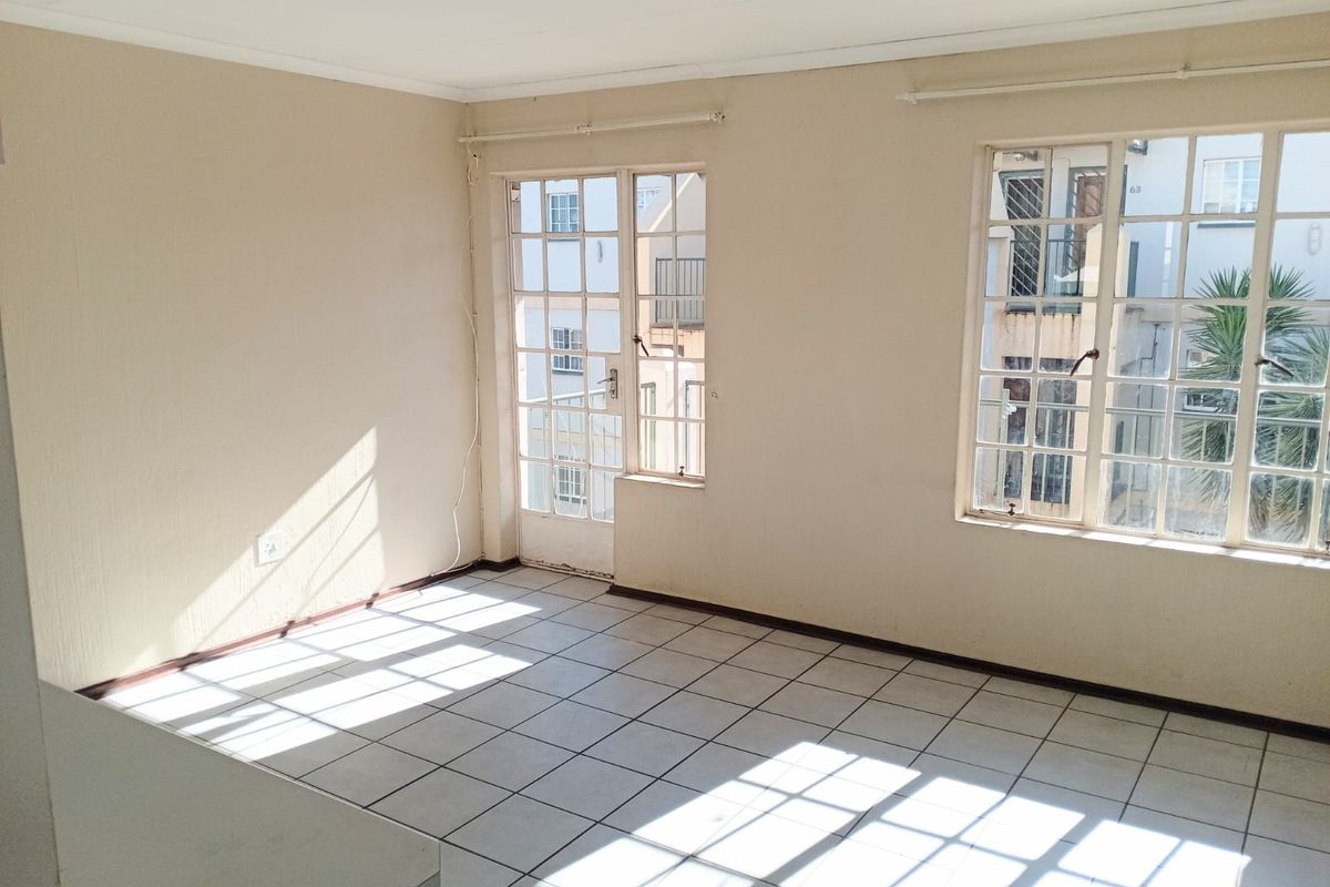 A bright, empty living area featuring tiled flooring, large windows, and a glass-paneled door leading to an outdoor space.