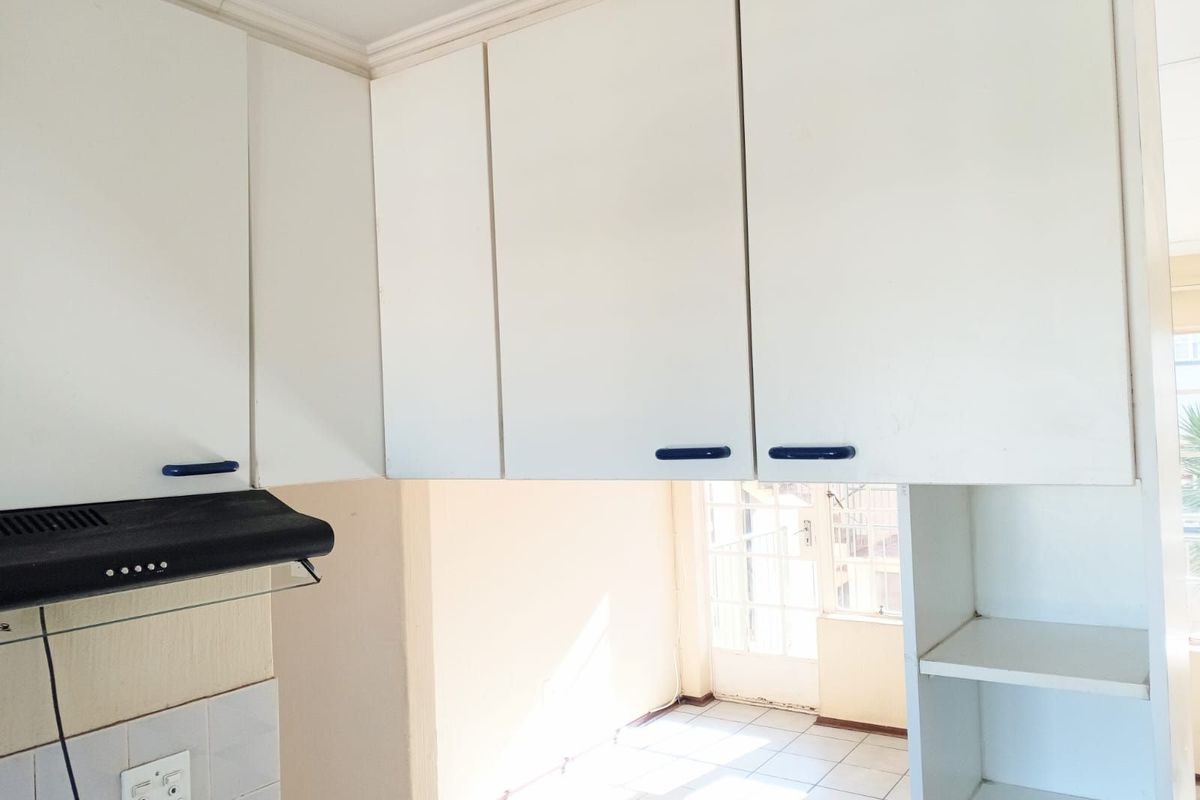 A functional kitchen area featuring white cabinetry, a built-in extractor fan, and tiled flooring, offering a bright and practical workspace.
