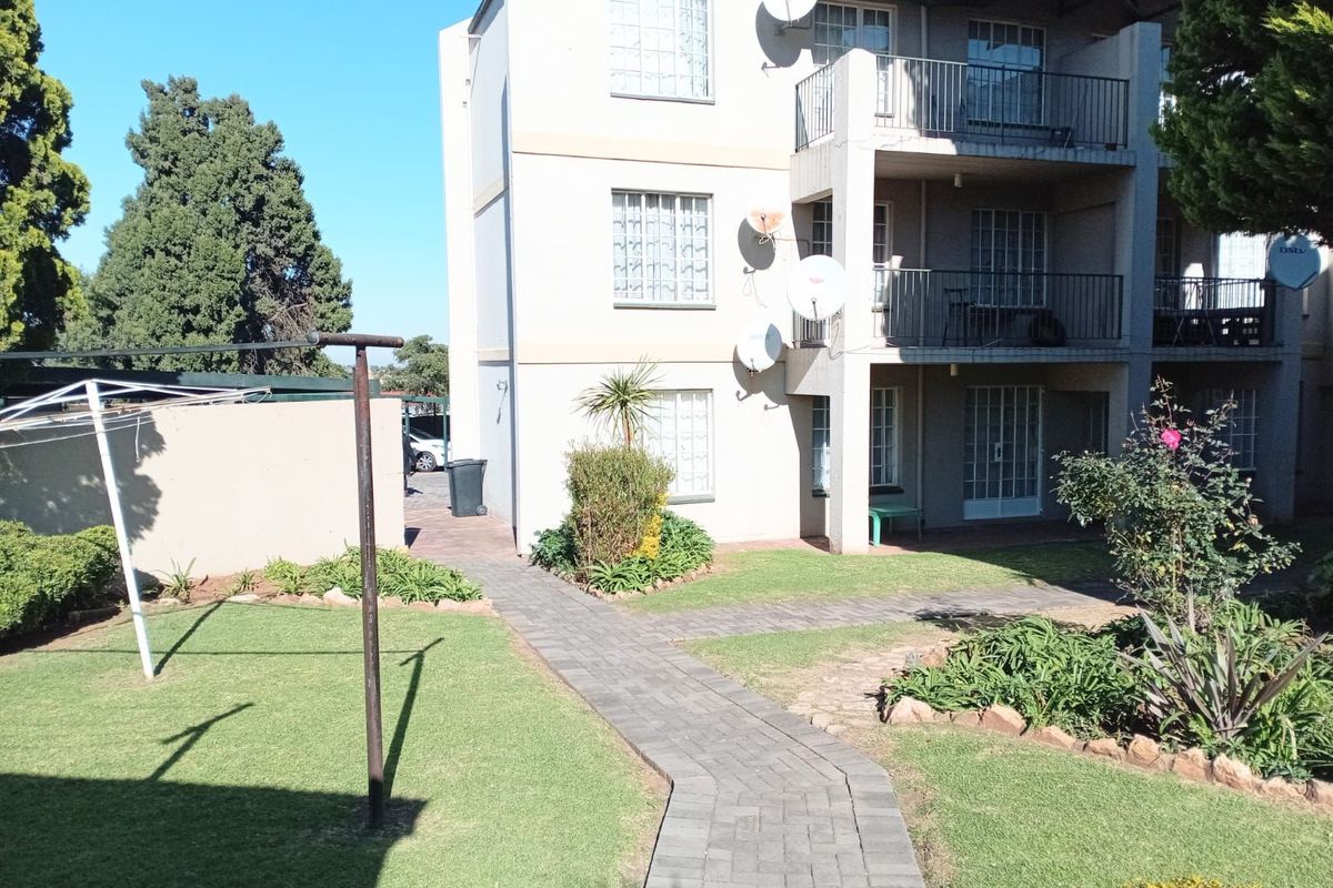 Exterior view of an apartment building featuring a paved walkway, landscaped garden area, and private balconies with metal railings.
