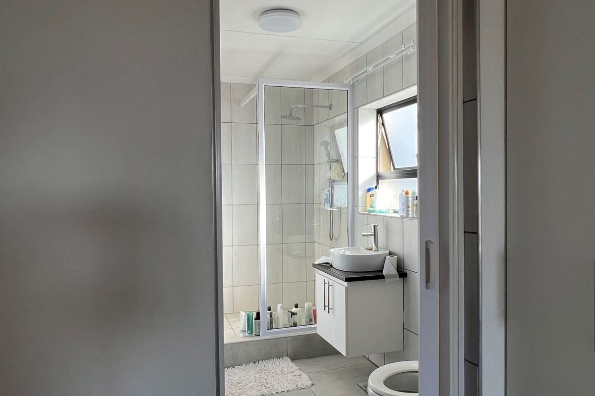 A functional bathroom featuring a walk-in shower with glass enclosure, a wall-mounted vanity with a vessel sink, and tiled flooring.