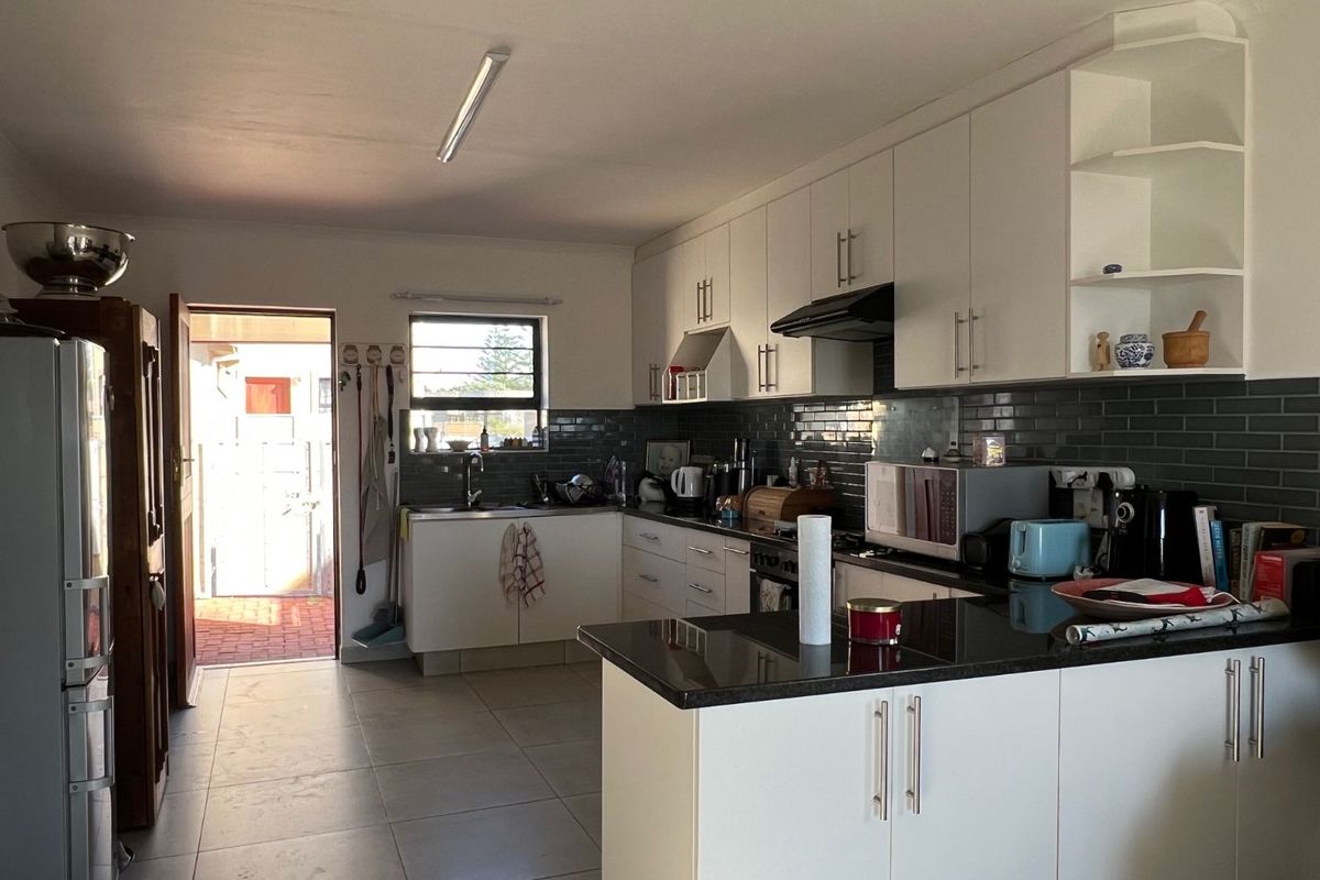 A functional kitchen featuring white cabinetry, dark granite countertops, a subway tile backsplash, and direct access to an outdoor patio area.