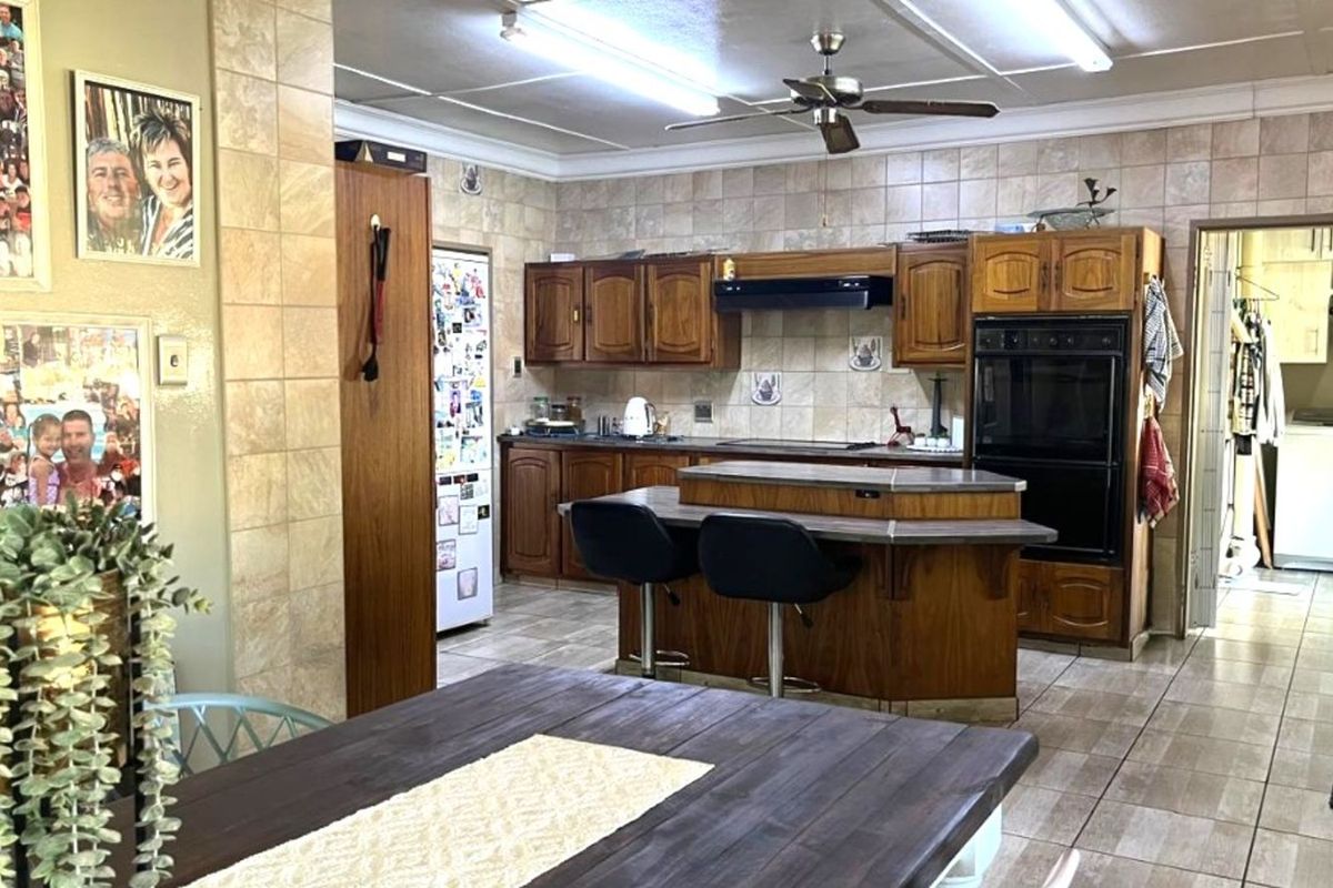 A spacious kitchen featuring traditional wooden cabinetry, a central breakfast bar, built-in oven, and tiled flooring throughout.