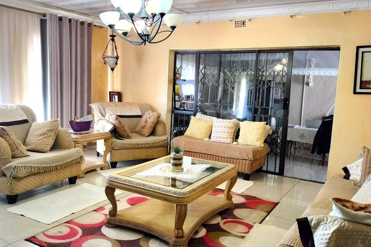 Spacious living room featuring tiled flooring, decorative ceiling cornicing, and sliding security doors leading to an adjacent patio area.