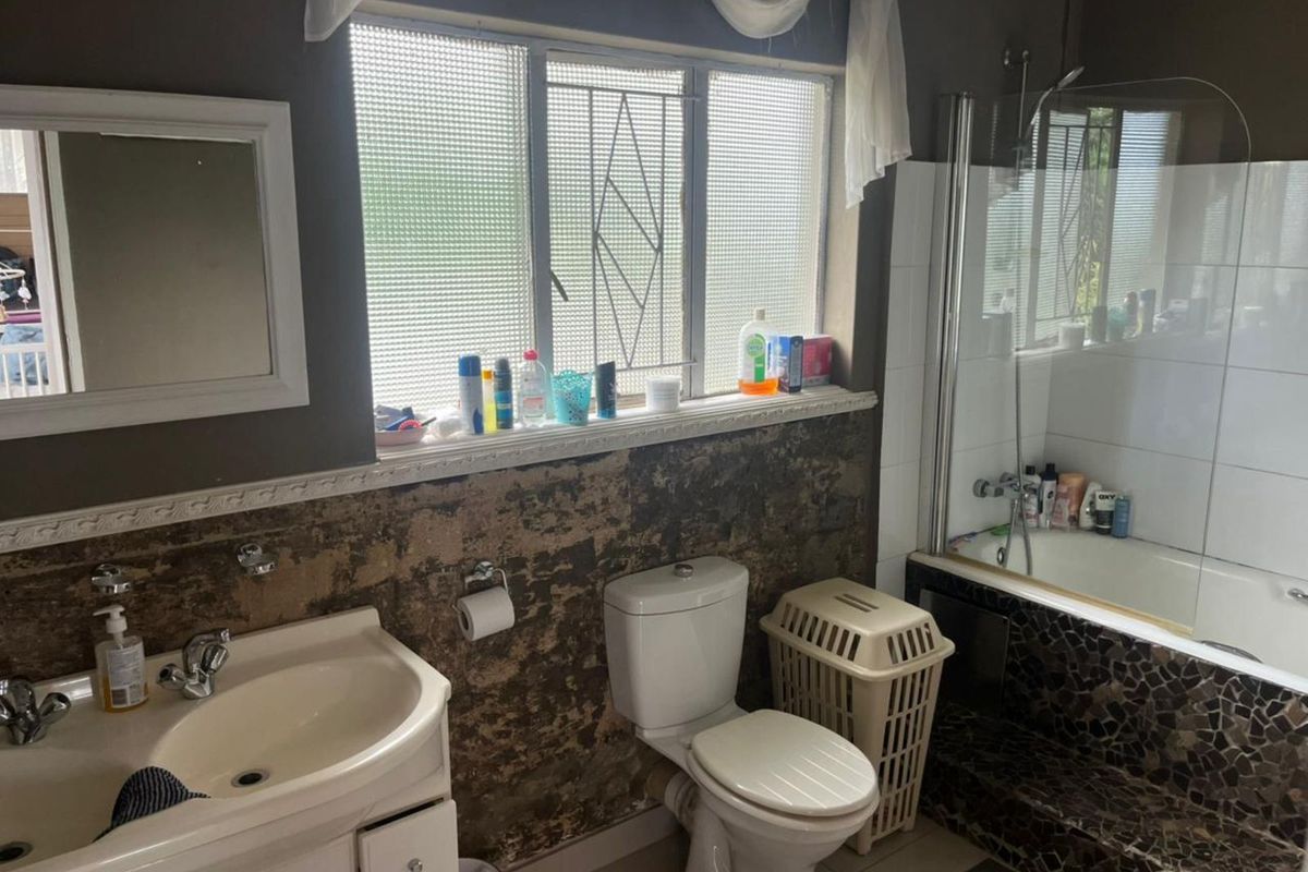 A bathroom featuring a built-in bathtub with mosaic tiling, a pedestal basin, and a toilet, currently requiring significant wall surface repairs and cosmetic updates.