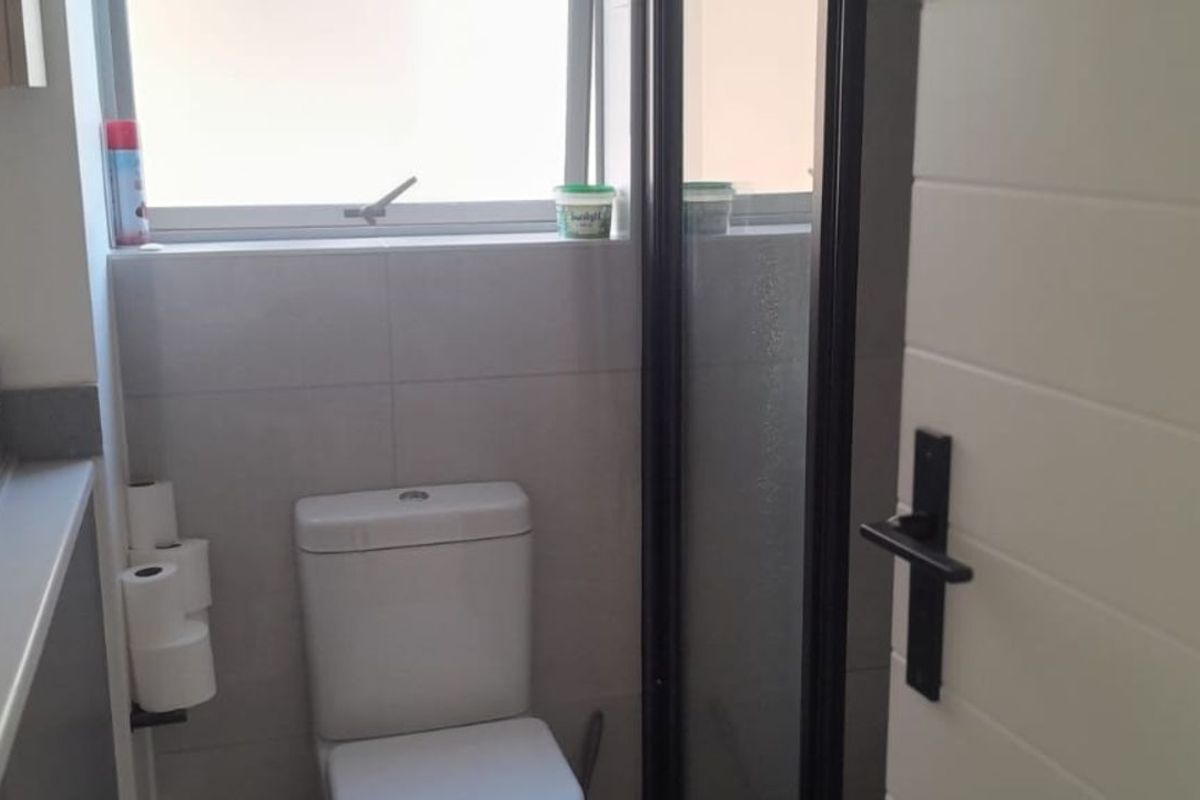 A functional bathroom featuring a toilet, a vanity with a basin, and a shower enclosure with a dark frame.
