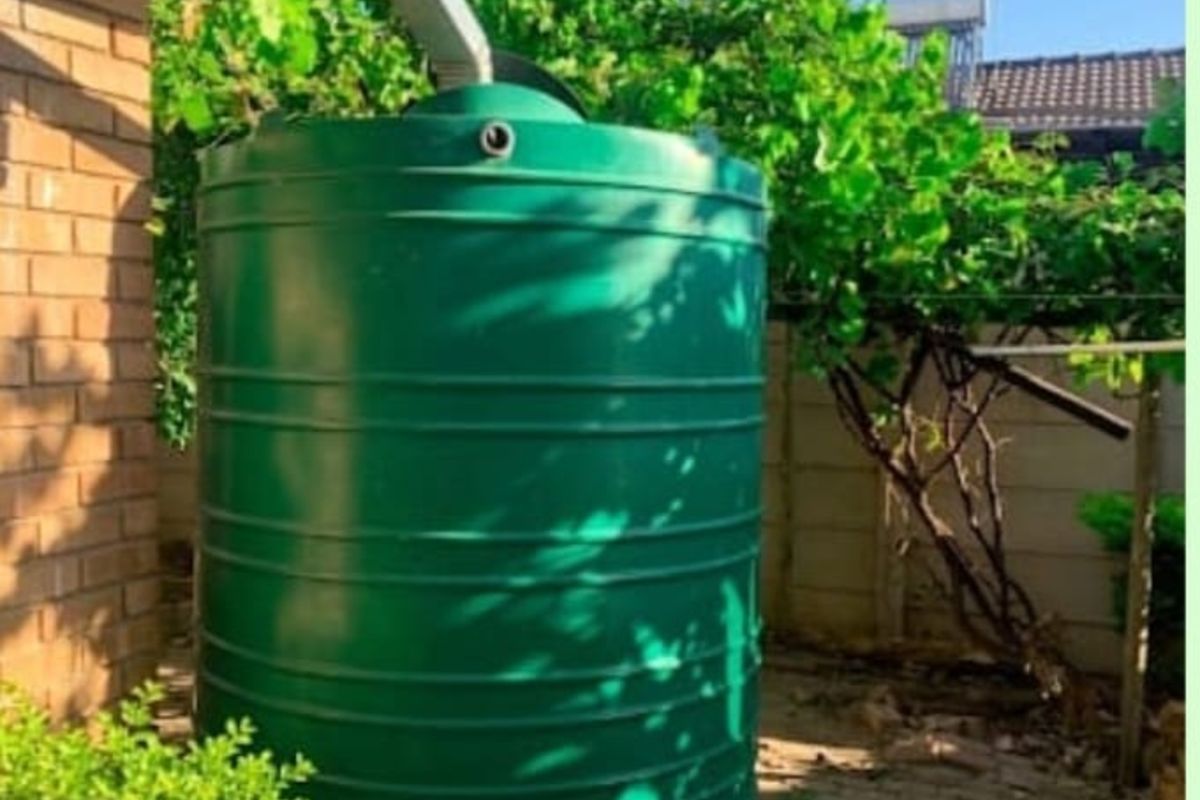 A green plastic water storage tank installed in the rear garden, connected to the building's gutter system for rainwater harvesting.