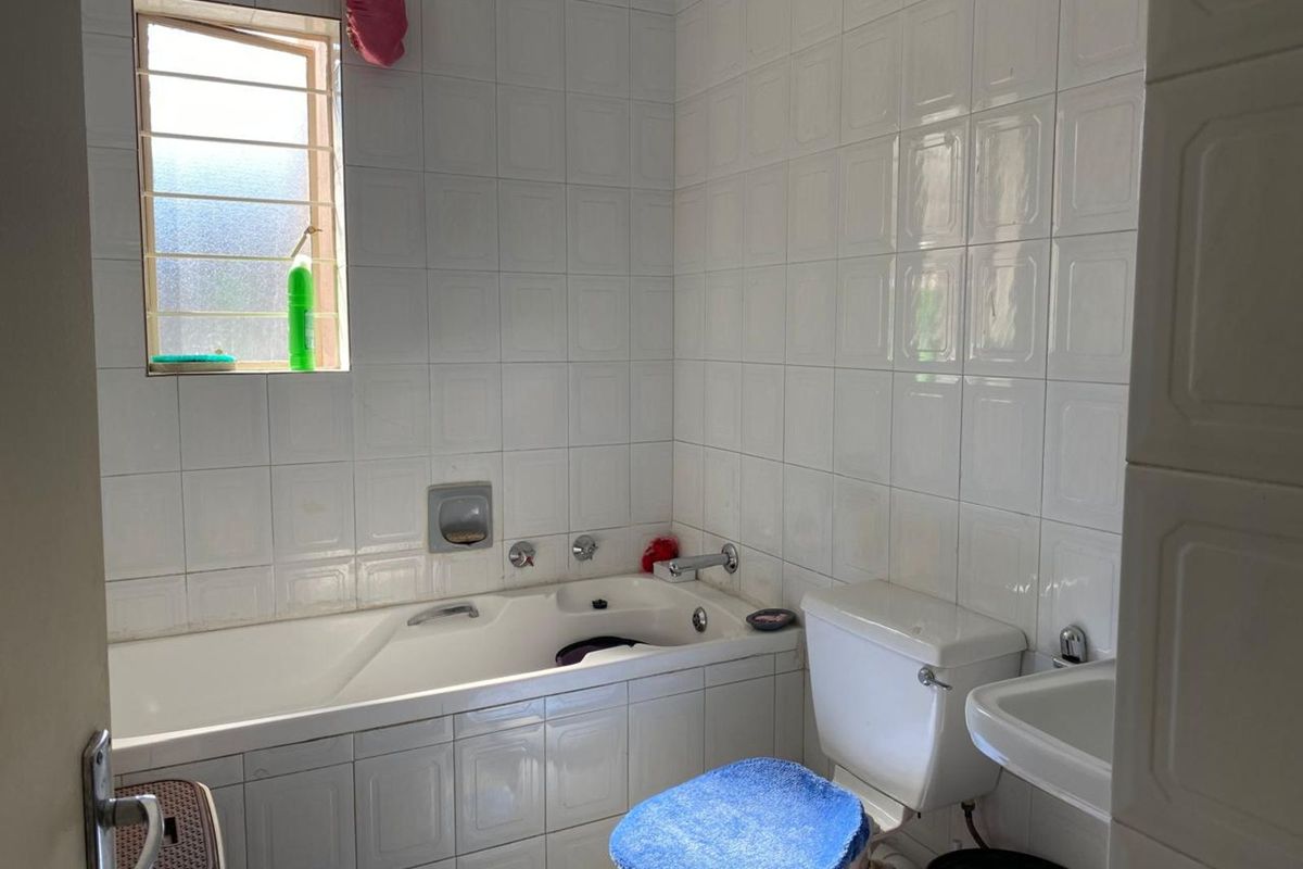 A functional bathroom featuring a built-in bathtub, wall-mounted basin, and toilet, finished with classic white wall tiles and a window for natural light.