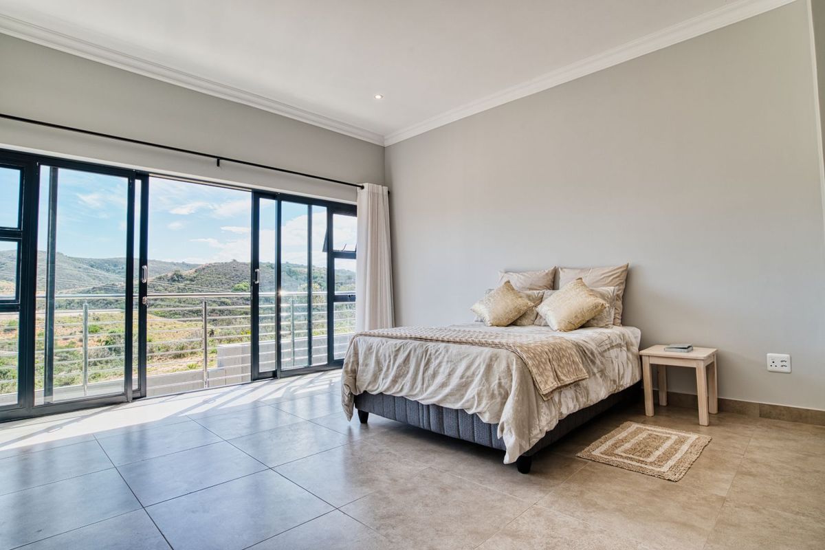 Spacious bedroom featuring large sliding glass doors that open onto a balcony with scenic landscape views and neutral tiled flooring.