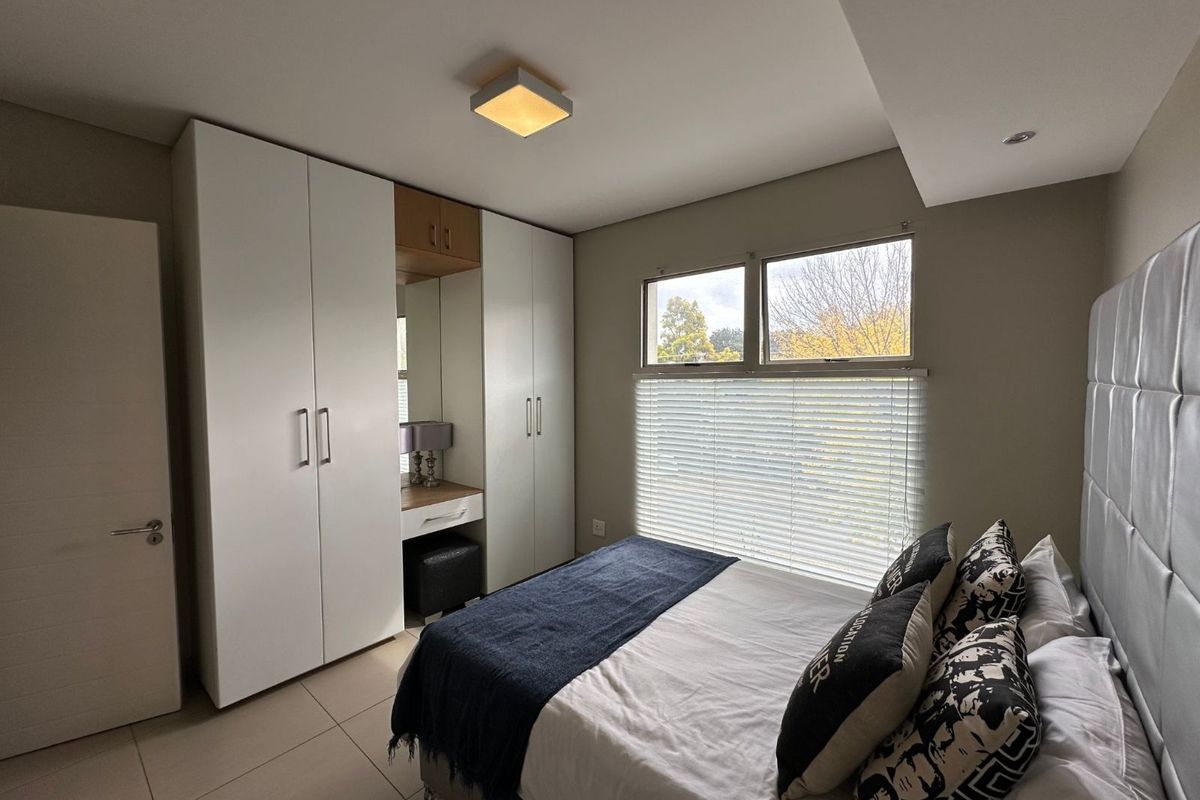 A well-maintained bedroom featuring built-in floor-to-ceiling wardrobes with an integrated vanity station, tiled flooring, and large windows with fitted blinds.