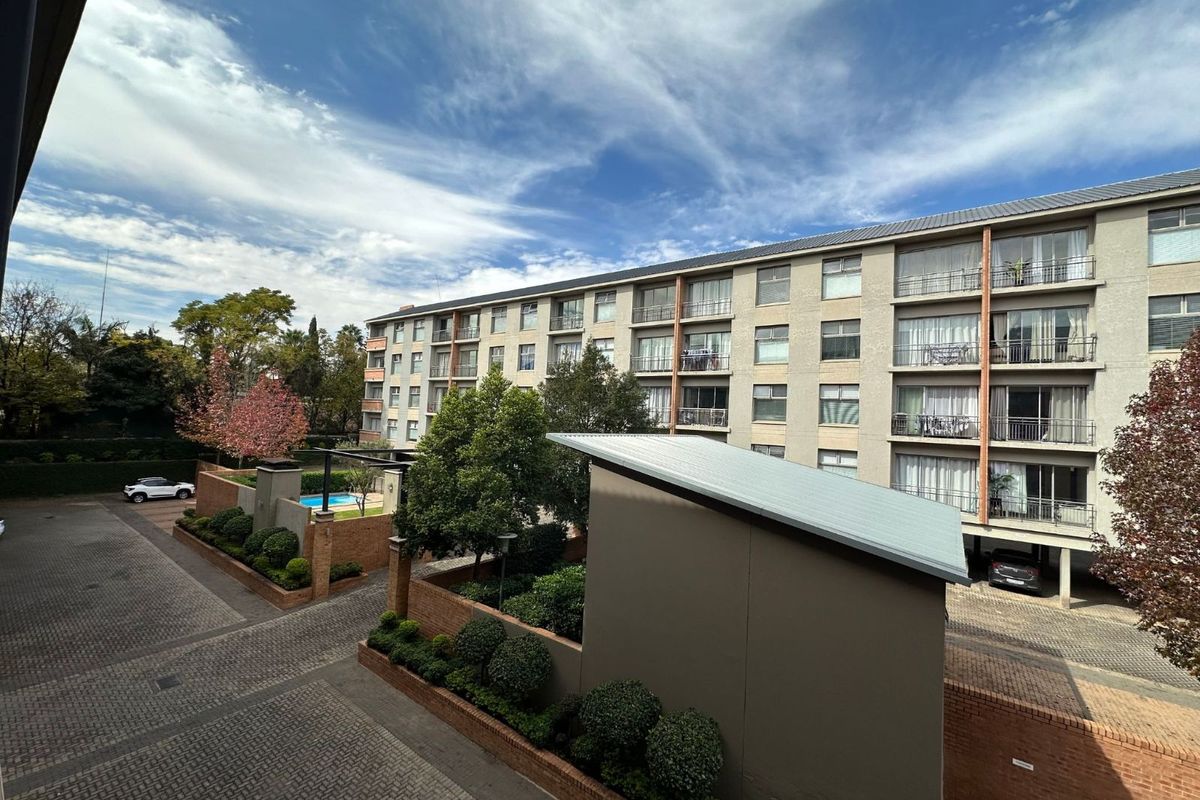An elevated view of the apartment complex exterior, featuring paved driveways, landscaped garden beds, and a communal pool area.
