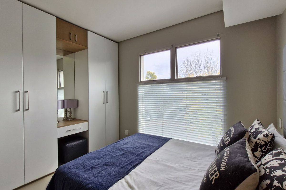A well-maintained bedroom featuring built-in white cabinetry with an integrated vanity and mirror, complemented by large windows with fitted blinds.