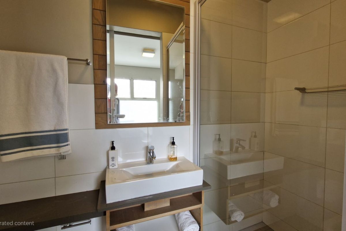 A modern bathroom featuring a wall-mounted vanity with a vessel sink, a framed mirror, and a glass-enclosed shower with tiled walls.