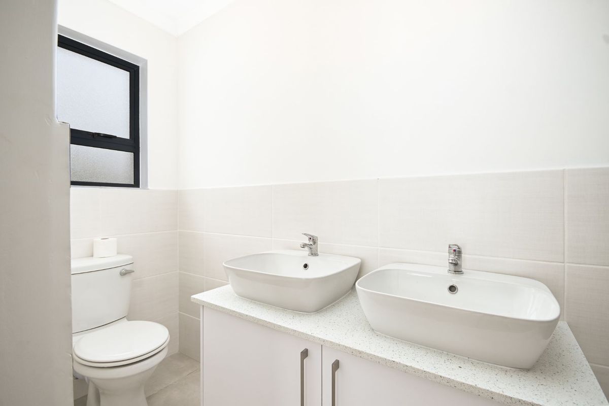 A clean, modern bathroom featuring a double vanity with vessel sinks, stone-look countertop, white cabinetry, and a low-flush toilet.